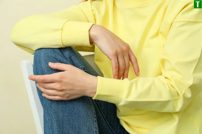 Скутість у коліні у спокої — ознака запалення або дефіциту синовіальної рідини Людина сидить на стільці й тримає коліно руками — відчуття скутості та дискомфорту у суглобі у стані спокою